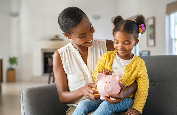 A mother showing her daughter a piggy bank.