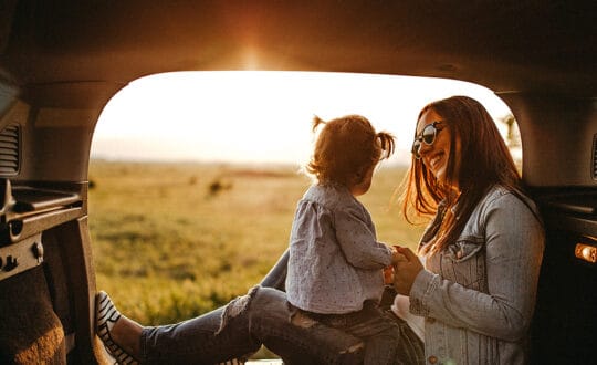 Mother and child smiling in the back of their car at sunset