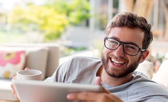 Guy smiling at camera with coffee and tablet in living space