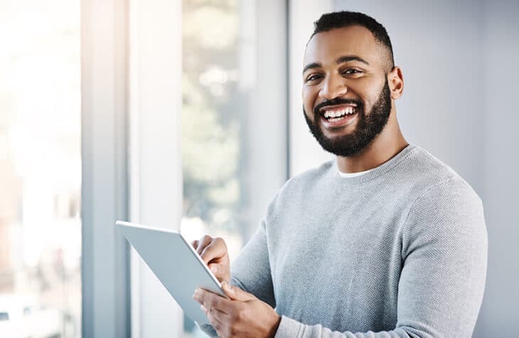 A man smiling while holding a tablet.