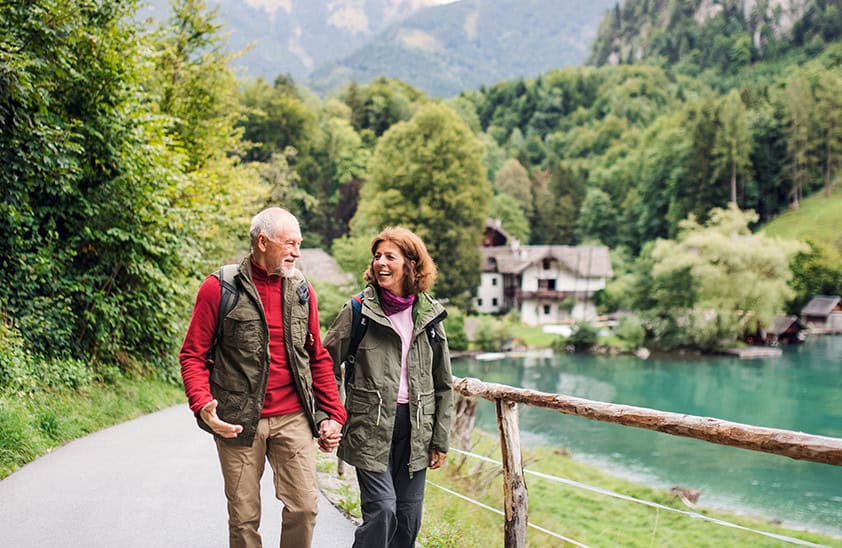 An older couple walking hand in hand on a trail.