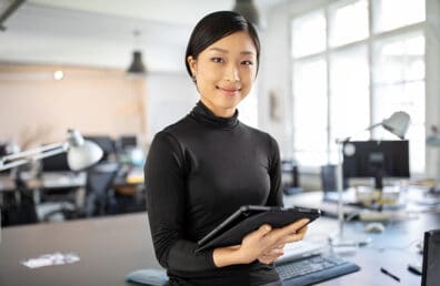 a woman standing in an office space and holding a notepad.