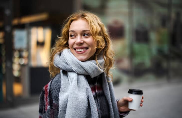 A young woman holding a coffee cup while walking and smiling.