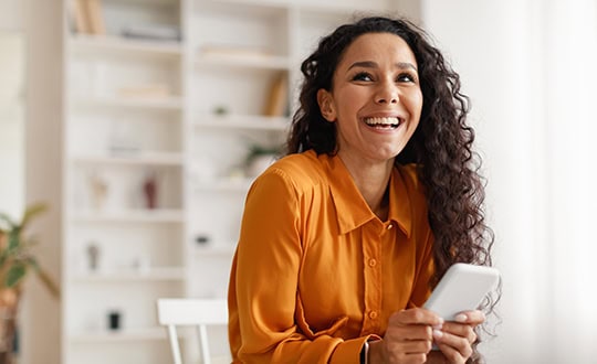 A woman smiling happily while holding a mobile device.