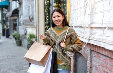 A woman smiling happily outside with her shopping bags.