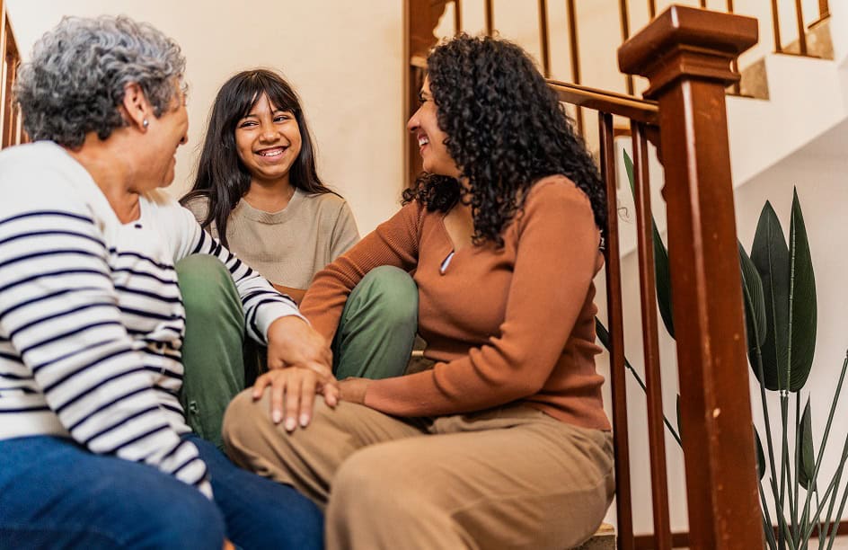 Three generations of women sitting on steps inside home.