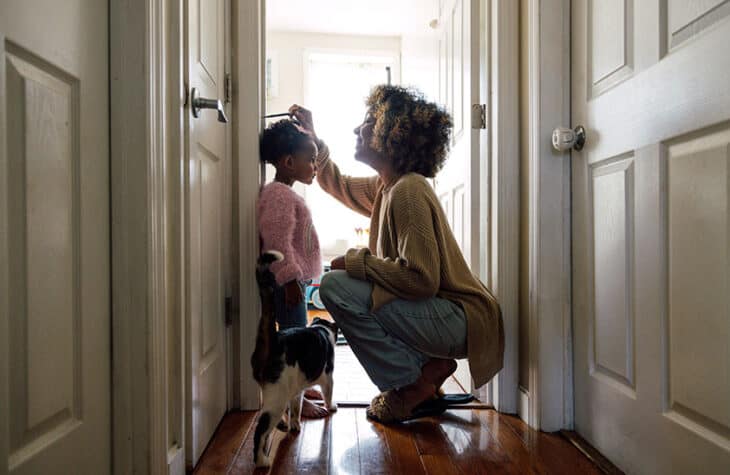 Mother measuring daughter's height and marking on wall at home
