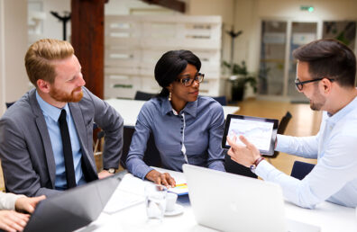 team meeting of three colleagues reviewing business performance charts on tablet