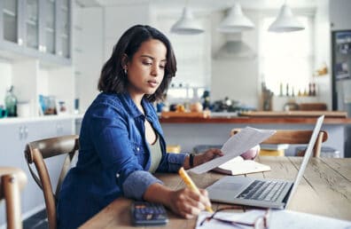 An older woman planning her budget while sitting at her kitchen table.