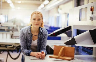 A young woman at a workstation, smiling kindly at the camera.