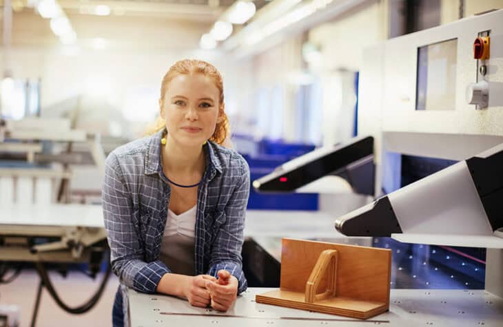 A young woman at a workstation, smiling kindly at the camera.