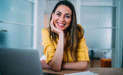 Woman at a desk smiling while using her laptop.