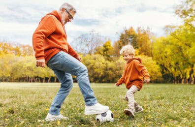 Happy family grandfather and grandson play football on lawn in park