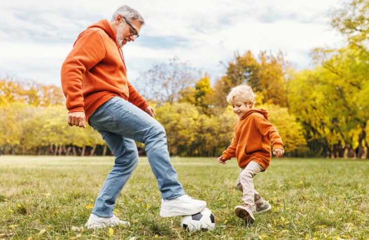 Happy family grandfather and grandson play football on lawn in park