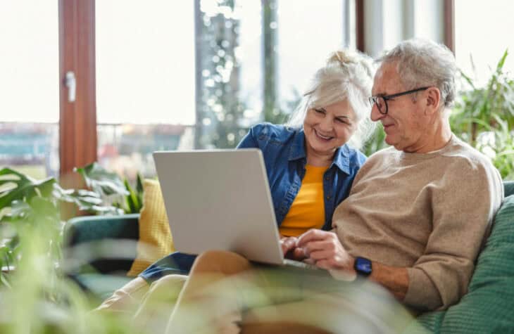Senior couple using laptop while sitting on sofa in living room at home.