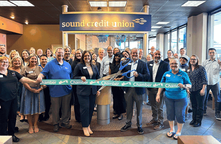 Members and employees of Sound Credit Union pose behind a ribbon for the opening of a new branch.